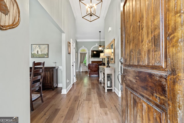 entrance foyer with wood finished floors, a chandelier, baseboards, crown molding, and a towering ceiling