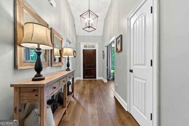 entrance foyer with hardwood / wood-style floors, a chandelier, vaulted ceiling, and baseboards