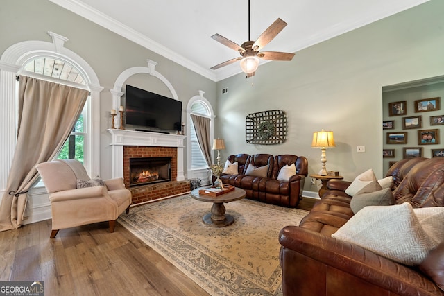 living room featuring plenty of natural light, wood finished floors, a ceiling fan, crown molding, and a fireplace