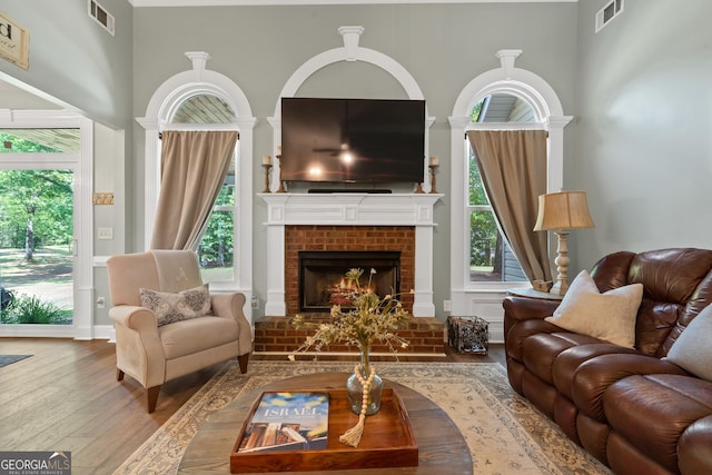 living room featuring hardwood / wood-style floors, plenty of natural light, a high ceiling, and a brick fireplace