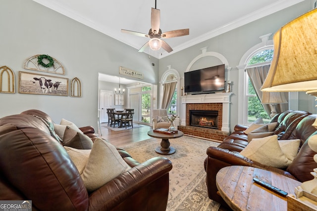 living room with crown molding, a ceiling fan, wood finished floors, a brick fireplace, and a towering ceiling