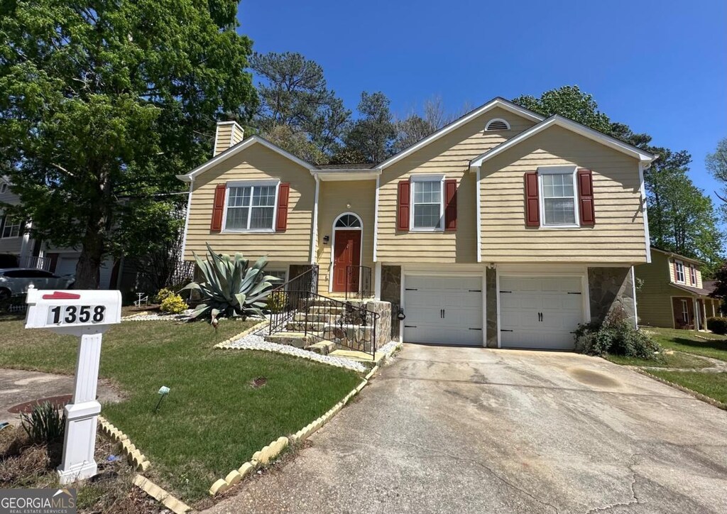 raised ranch with concrete driveway, an attached garage, a chimney, and a front lawn