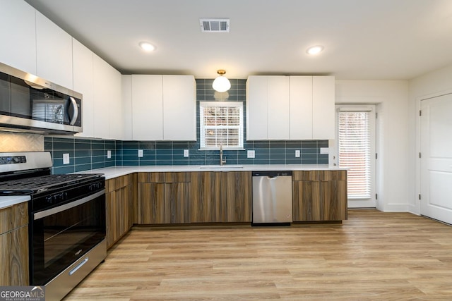 kitchen featuring light wood-style floors, modern cabinets, light countertops, a sink, and appliances with stainless steel finishes