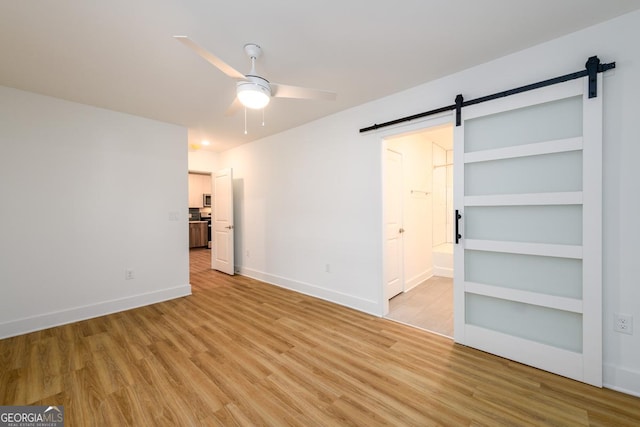 unfurnished bedroom with light wood-type flooring, a barn door, baseboards, and connected bathroom