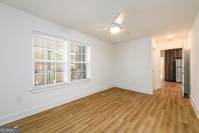 empty room with baseboards, a ceiling fan, and light wood-style flooring