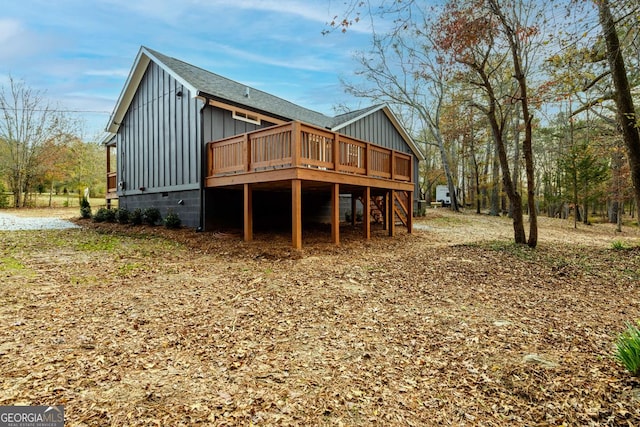 rear view of house featuring roof with shingles, a wooden deck, board and batten siding, and stairway