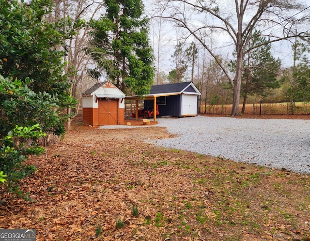 view of yard with a storage unit, an outdoor structure, fence, and gravel driveway