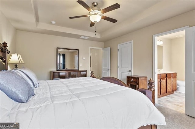 bedroom featuring light colored carpet, a ceiling fan, ensuite bath, and a tray ceiling
