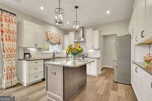 kitchen featuring backsplash, appliances with stainless steel finishes, wall chimney exhaust hood, and light wood-type flooring