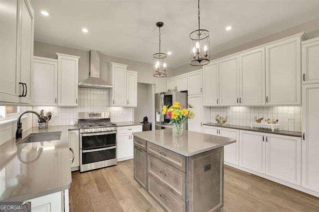 kitchen featuring backsplash, appliances with stainless steel finishes, a sink, a chandelier, and wall chimney exhaust hood
