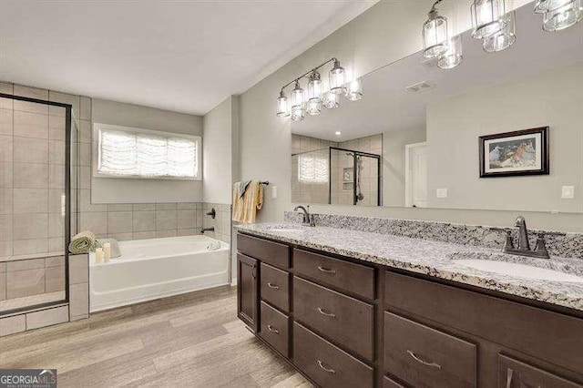 bathroom with a stall shower, a sink, a bath, and wood finished floors
