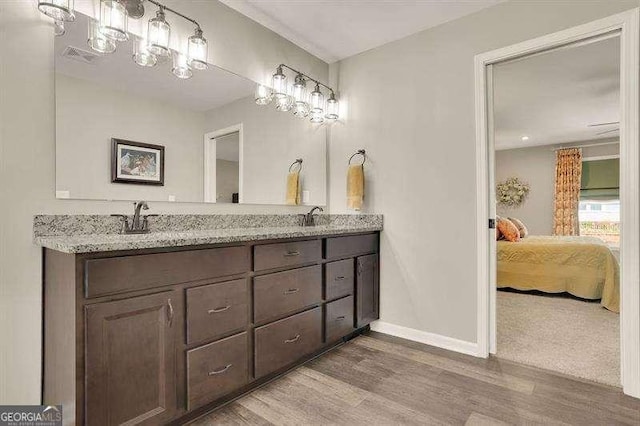 ensuite bathroom featuring double vanity, wood finished floors, a sink, baseboards, and connected bathroom