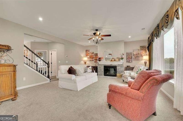 living room with a fireplace, light carpet, baseboards, stairway, and a ceiling fan