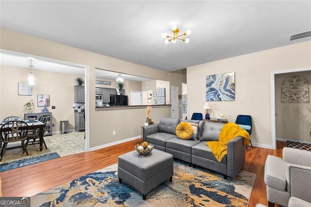 living area featuring visible vents, baseboards, wood finished floors, and a notable chandelier