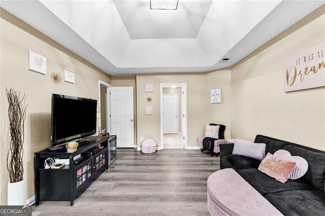 living room featuring baseboards, a tray ceiling, wood finished floors, and visible vents