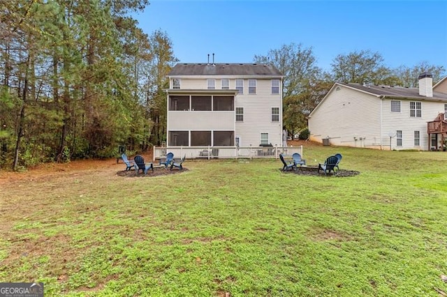 back of house featuring a lawn, a sunroom, and an outdoor fire pit