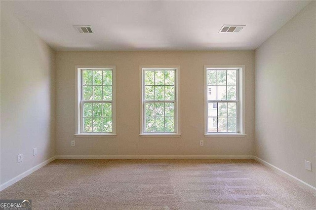empty room with light colored carpet, visible vents, and a healthy amount of sunlight