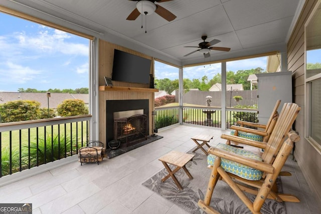 sunroom with plenty of natural light, a ceiling fan, and a lit fireplace
