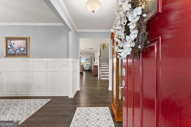 foyer entrance featuring dark wood-style flooring, crown molding, stairway, a wainscoted wall, and a decorative wall
