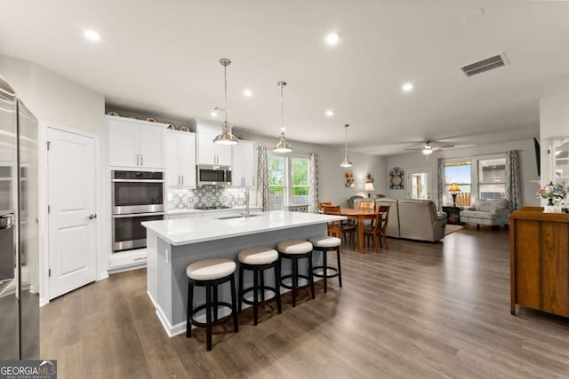kitchen featuring white cabinets, appliances with stainless steel finishes, a kitchen island with sink, decorative backsplash, and visible vents