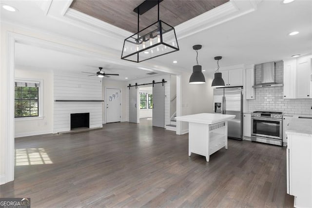kitchen with light countertops, a barn door, wall chimney exhaust hood, a ceiling fan, and stainless steel appliances
