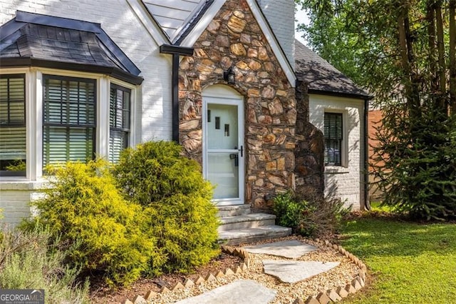 property entrance with a chimney, a yard, brick siding, and stone siding