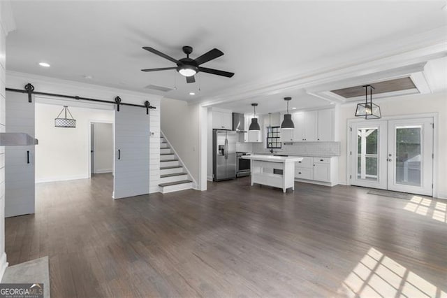 unfurnished living room with ceiling fan, crown molding, a barn door, recessed lighting, and dark wood-type flooring