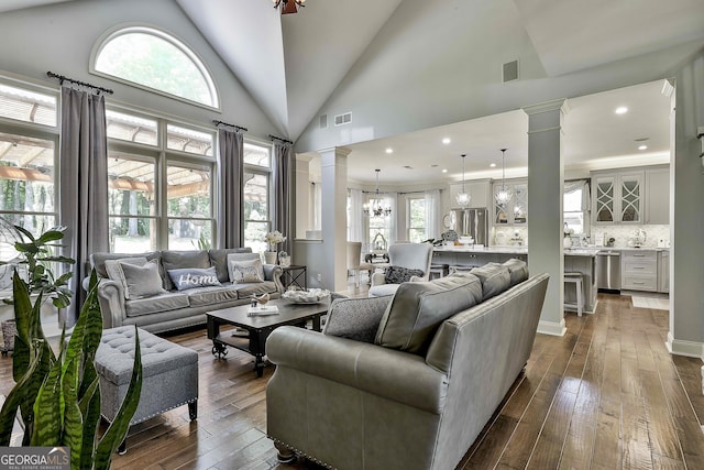 living area featuring dark wood-style flooring, a notable chandelier, lofted ceiling, ornate columns, and visible vents