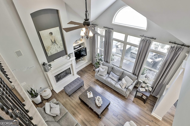 living area featuring ceiling fan, arched walkways, high vaulted ceiling, wood finished floors, and a high end fireplace