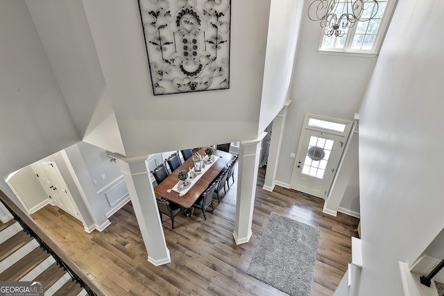 entrance foyer featuring a towering ceiling, wood finished floors, baseboards, an inviting chandelier, and ornate columns