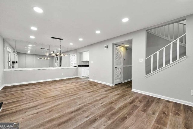 unfurnished living room with baseboards, recessed lighting, wood finished floors, and a notable chandelier