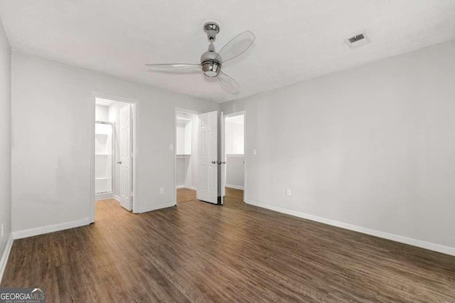 unfurnished bedroom featuring visible vents, wood finished floors, baseboards, a spacious closet, and a ceiling fan