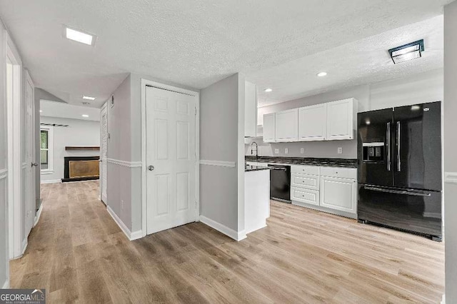 kitchen featuring dark countertops, light wood-type flooring, a textured ceiling, white cabinetry, and black appliances