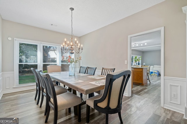 dining room featuring a wainscoted wall, plenty of natural light, light wood finished floors, a chandelier, and a textured ceiling
