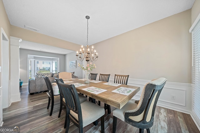 dining area with dark wood-type flooring, wainscoting, and a chandelier