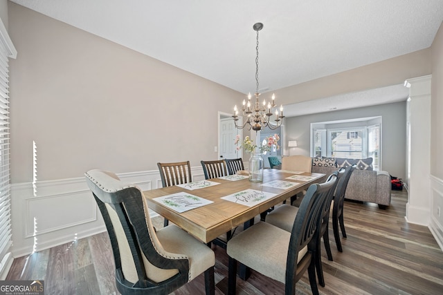 dining area with wood finished floors, a chandelier, wainscoting, and a decorative wall
