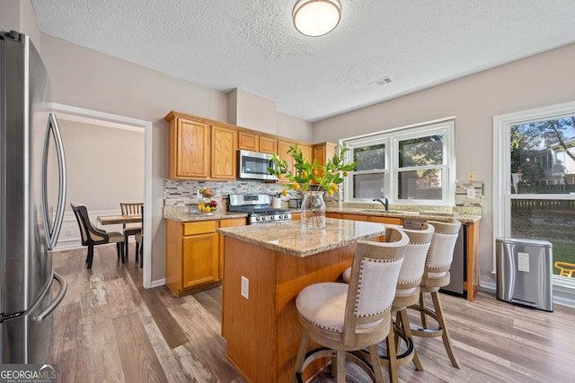 kitchen with appliances with stainless steel finishes, backsplash, a sink, light wood-style floors, and a textured ceiling