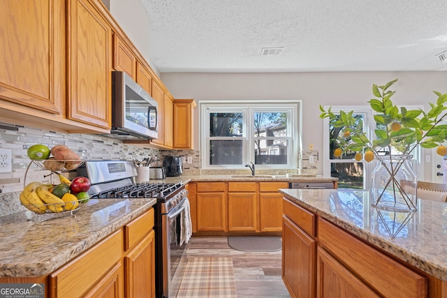 kitchen featuring stainless steel appliances, a sink, a textured ceiling, backsplash, and light stone countertops