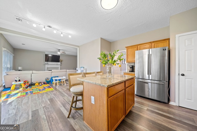 kitchen with freestanding refrigerator, wood finished floors, a fireplace, light stone counters, and a kitchen island