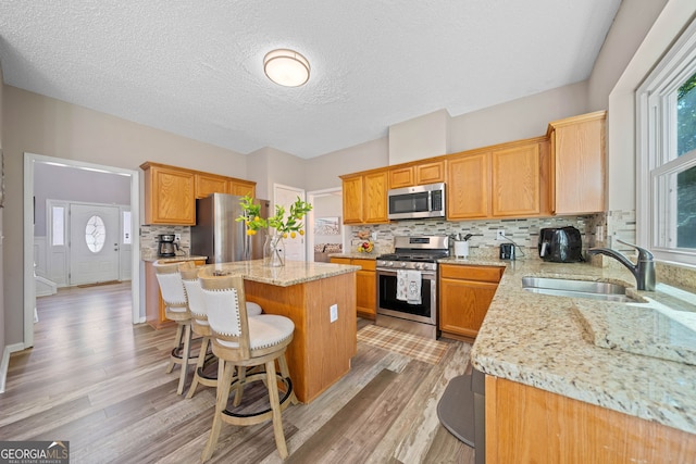 kitchen with appliances with stainless steel finishes, a sink, a kitchen island, tasteful backsplash, and light wood-type flooring