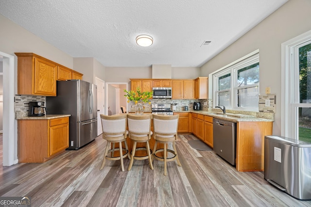 kitchen featuring appliances with stainless steel finishes, decorative backsplash, light wood finished floors, a textured ceiling, and a kitchen bar