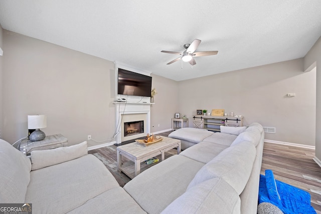 living area featuring a ceiling fan, wood finished floors, baseboards, and a fireplace