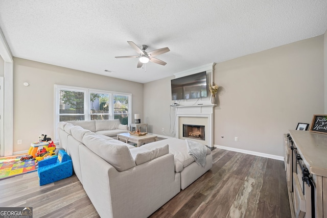 living room with a ceiling fan, dark wood-style flooring, a textured ceiling, a fireplace, and baseboards