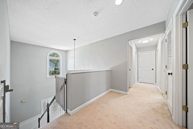 hallway featuring an upstairs landing, a textured ceiling, carpet, and baseboards