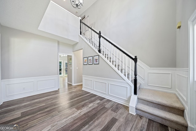 stairs featuring a decorative wall, wood finished floors, wainscoting, healthy amount of natural light, and a chandelier