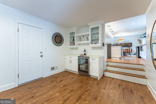 indoor bar featuring beverage cooler, wood finished floors, baseboards, crown molding, and hanging light fixtures