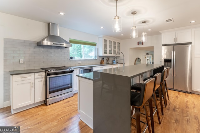 kitchen with stainless steel appliances, wall chimney range hood, dark countertops, a center island, and recessed lighting