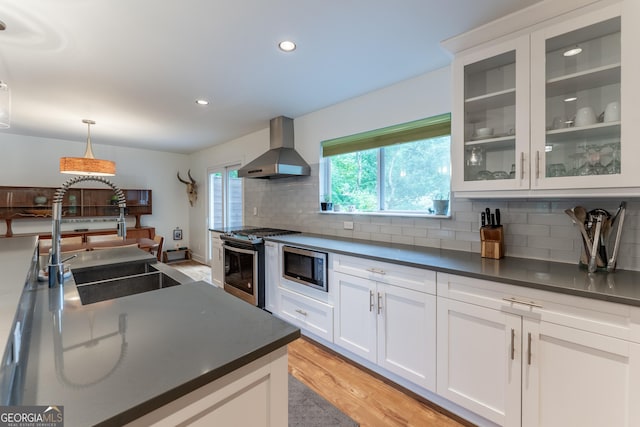 kitchen featuring wall chimney range hood, appliances with stainless steel finishes, a sink, dark countertops, and recessed lighting