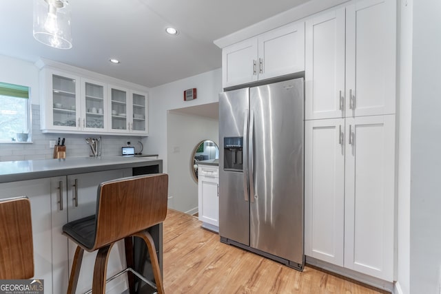 kitchen with stainless steel fridge with ice dispenser, decorative backsplash, glass insert cabinets, light wood-style flooring, and white cabinetry
