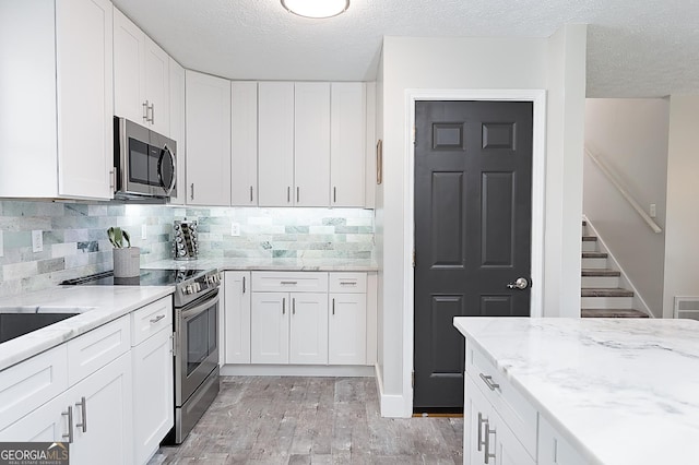 kitchen featuring decorative backsplash, appliances with stainless steel finishes, light stone countertops, white cabinets, and light wood-style floors